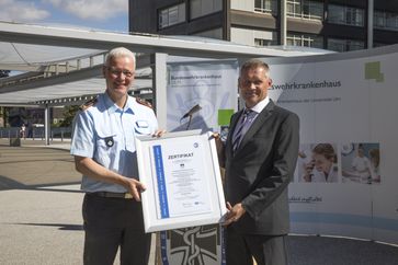 Generalarzt Dr. Jörg Ahrens vom BwKrhs Ulm empfängt das Zertifikat von Kurt Schumacher, Bereichsleiter vom TÜV Süd.  Bild: Presse- und Informationszentrum des Sanitätsdienstes der Bundeswehr Fotograf: Bundeswehr/Silicya Roth