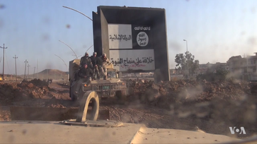 Iraqi soldiers drive past an ISIL sign in eastern Mosul, January 2017