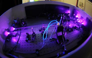 Innerhalb der vier Resonatorspiegel überhöhen sich die ultravioletten Lichtpulse fortlaufend. Die verschränkten Photonen werden von einem Kristall, der sich im schwarzen Gehäuse befindet (mit blauen Schläuchen verbunden), erzeugt. Bild: Thorsten Naeser