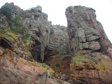 Ansicht der Fundstelle La Cotte de St Brelade auf der Insel Jersey, Großbritannien. Ein Großteil der Knochen stammt aus den Ausgrabungen unter dem Granitbogen links im Bild ist. Quelle: Foto: Geoff Smith, MONREPOS (idw)