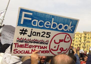 A man during the 2011 Egyptian protests carrying a card saying "Facebook,#jan25, The Egyptian Social Network"