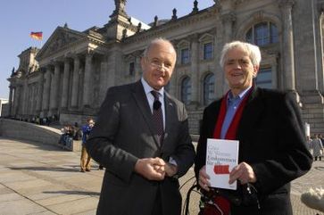 Hans-Christian Ströbele (rechts) nimmt sein persönliches Exemplar entgegen und hebt den Freiheitsgedanken des bedingungslosen Grundeinkommens hervor. Quelle: Universität Karlsruhe (TH) - Interfakult