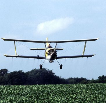 Flugzeug, welches Insektizide über einem Feld versprüht. Diese Form der Pflanzenschutzmittelapplikation ist in der EU verboten