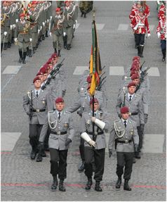 Fallschirmjäger im Großen Dienstanzug mit bordeauxrotem Barett und grüner Waffenfarbe. Vorne die Fahnenabordnung mit Truppenfahnen der Bundeswehr.