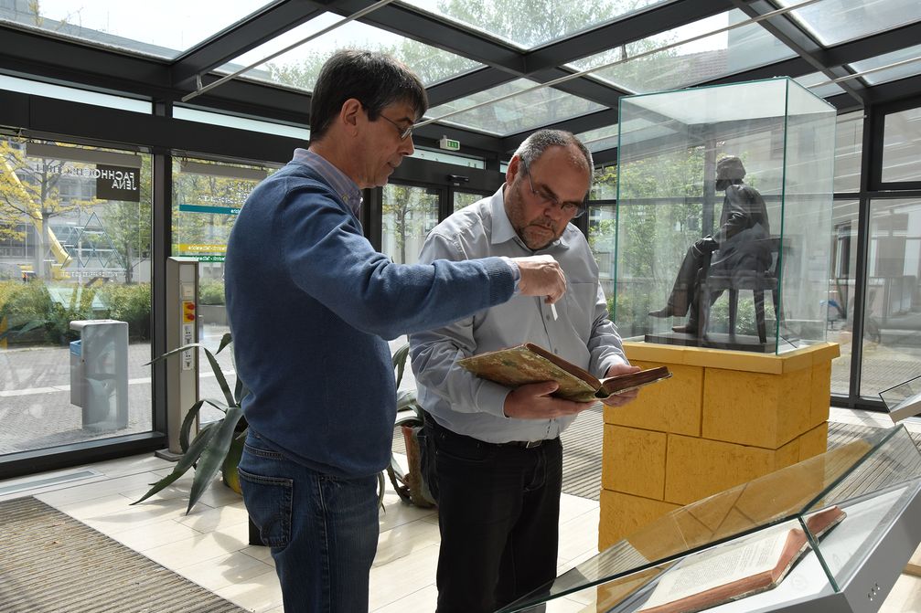 THULB-Werkstattleiter Frank Schieferdecker, li., und Rektor Steffen Teichert mit Newtons Original vor dem ausgestellten Faksimile. Re.die Skulptur von Ernst Abbe, Dauerleihgabe von ZEISS für die EAH