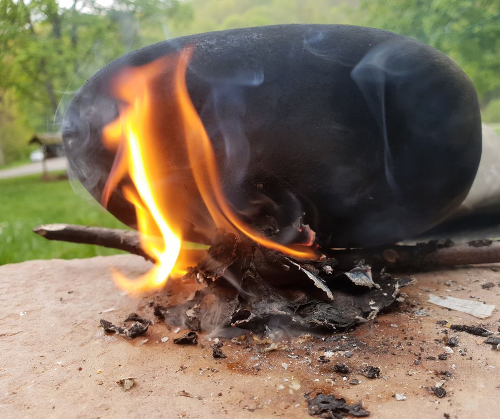 Experiment zur Herstellung von Birkenpech mithilfe von brennender Birkenrinde und einer glatten Oberfläche.