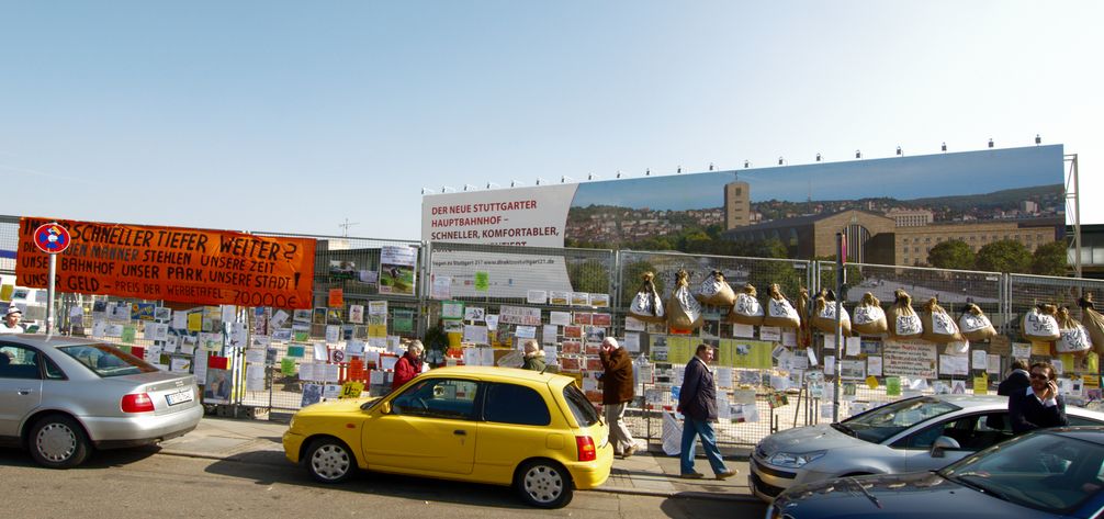 Großformatige Werbung für Stuttgart 21 im Bereich des ehemaligen Hauptbahnhof-Nordflügels. Im Vordergrund sind Teile des mit Kritik behängten Bauzauns zu sehen.