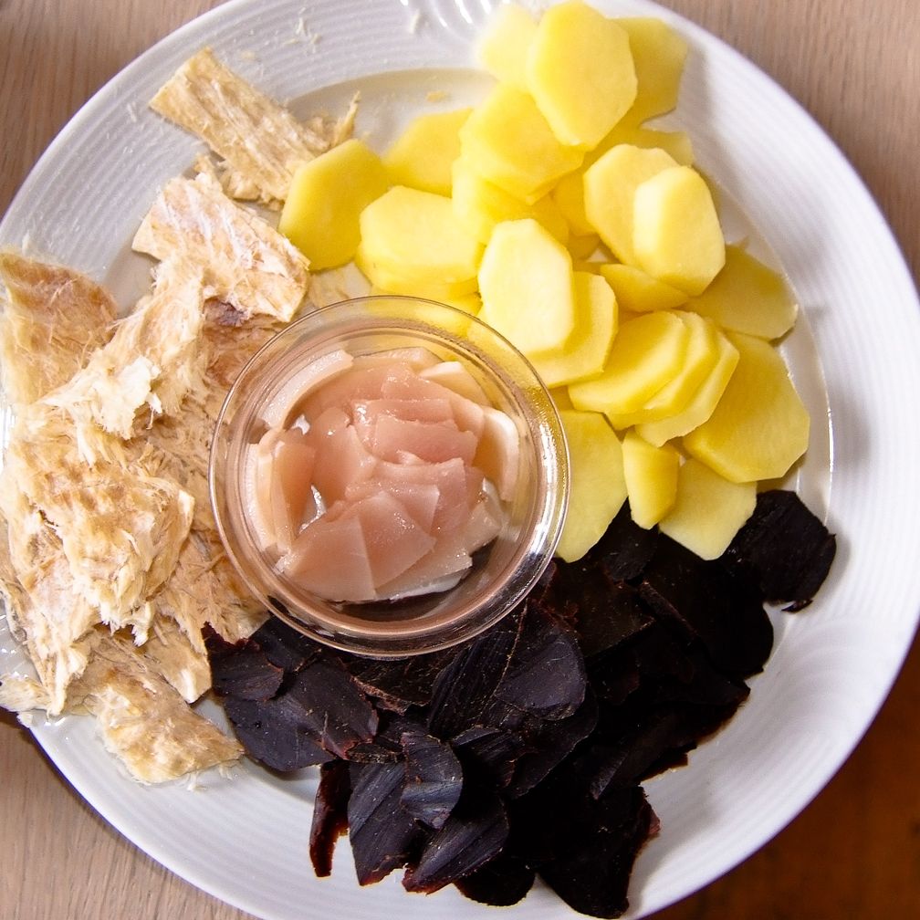 Tvøst og spik. Das schwarze Grindwalfleisch und Speck (in der Schale) wird gerne zusammen mit Trockenfisch (links) und Salzkartoffeln gereicht. Dazu trinkt man traditionell Bier