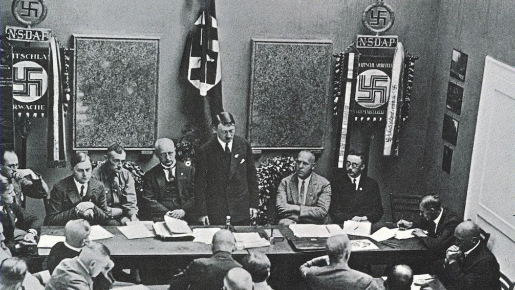 Adolf Hitler (Mitte) und der Publizist, "Russland-Experte" und künftige "Ostminister" Alfred Rosenberg als junger NSDAP-Funktionär bei einer Partei-Sitzung 1925 in München (dritter links von Hitler) Bild: www.globallookpress.com