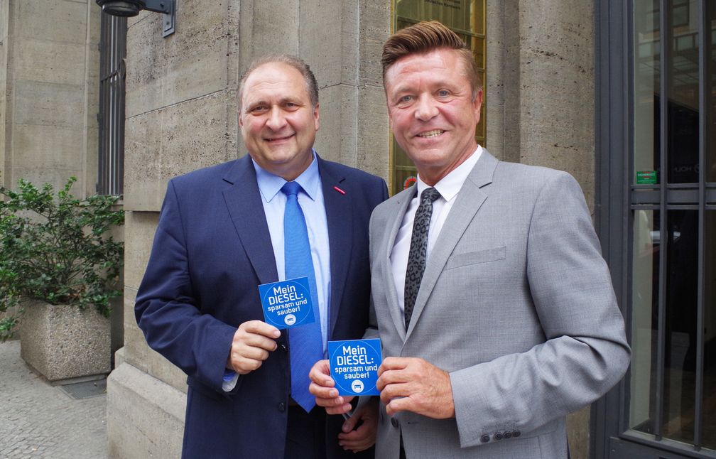 ZDH-Präsident Hans Peter Wollseifer und ZDK-Vizepräsident und Bundesinnungsmeister Wilhelm Hülsdonk präsentieren den Aufkleber des Kfz-Gewerbes "Mein Diesel: sparsam und sauber!" Bild: "obs/Zentralverband Deutsches Kraftfahrzeuggewerbe/Wagner/ZDH"