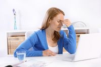 Eine Frau sitzt gestresst am Laptop mit Kopfschmerzen.
