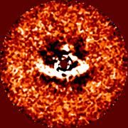 Dieses Bild der HiCIAO-Kamera am SUBARU-Teleskop bietet einen Blick auf die protoplanetaren Scheibe des jungen Sterns LkCa 15. Ein Teil der Scheibe (weiss) wird vom Stern (Mitte, dunkelrot maskiert) beleuchtet und so sichtbar gemacht. Deutlich zu erkennen ist die scharf definierte Innenkante der Scheibe, wo der Leerraum in ihrer Mitte anfängt. Die Aussparung ist unsymmetrisch – sie ist links deutlich größer als rechts – und dürfte auf einen oder mehrere neugeborene Planeten zurückgehen, die dort um den Stern umlaufen. Bild: MPIA (C. Thalmann) & NAOJ