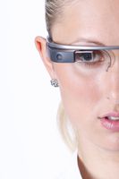 Datenbrille Google Glass (Explorer Edition 2014) auf dem Kopf eines Models. Erhöht vor dem Auge das Mini-Display zum Einblenden von Bewegtbildern, daneben die Kamera. Im hier nicht sichtbaren, daran anschließenden Bügel zum Ohr hin befinden sich Touchpad, Lautsprecher, Beschleunigungssensor und Computer.