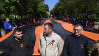 Der Chef der Donezker Volksrepublik, Denis Puschilin (links), führt eine Menschenkolonne bei einem Umzug mit einem 300 Meter langen St.-Georgs-Band in Mariupol während der Feierlichkeiten zum 77. Jahrestag des Sieges im Großen Vaterländischen Krieg an, 9. Mai 2022