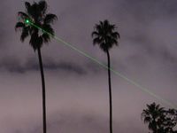 Der bei Nacht auf eine Palme gerichtete Strahl eines grünen 5-mW-Laserpointers.