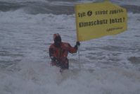 Orkan ueber der Insel Sylt. Greenpeace Aktivisten mit Banner "Sylt stirbt zuerst. Klimaschutz jetzt!" stehen im Wasser vor dem Strand. Der Sand wird durch den Sturm und das Hochwasser weggespuelt, massive Kuestenschaeden sind die Folge. Foto: Martin Langer/Greenpeace