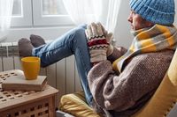 Man with hat, sweater and hand gloves indoors on a chilly winter day, energy and gas crisis, cold room, heating problems.