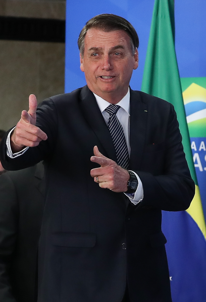 Bolsonaro im April 2019, mit seiner typischen Handgeste, die er schon während des Präsidentschaftswahlkampfs gerne benutzte. Aus Daumen und Mittelfinger formt er eine Pistole und drückt symbolisch ab.[36][37] Viele seiner Anhänger imitierten diese Geste.[38]
